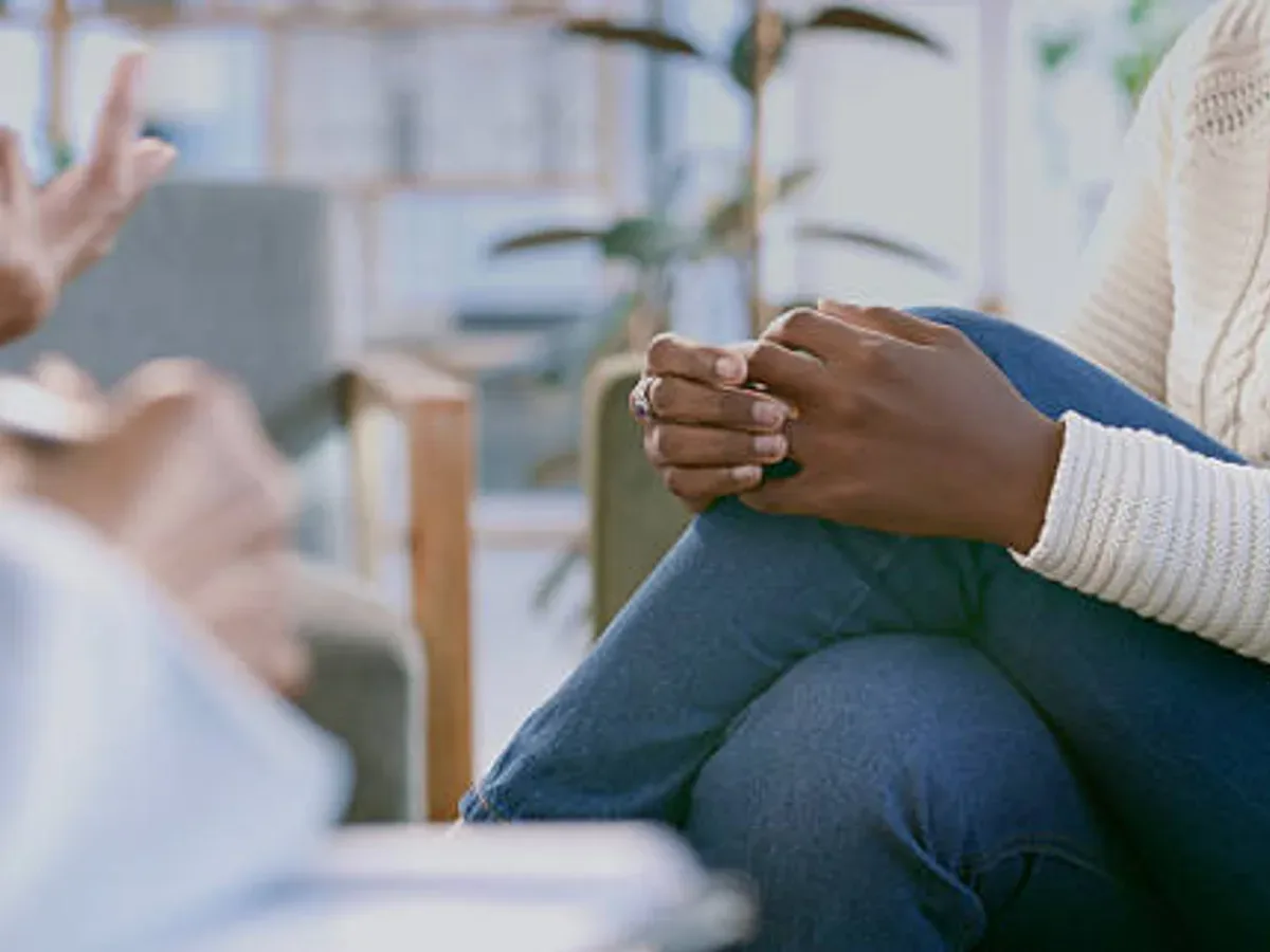 A patient with clasped hands listening intently while a therapist gestures during a counseling session